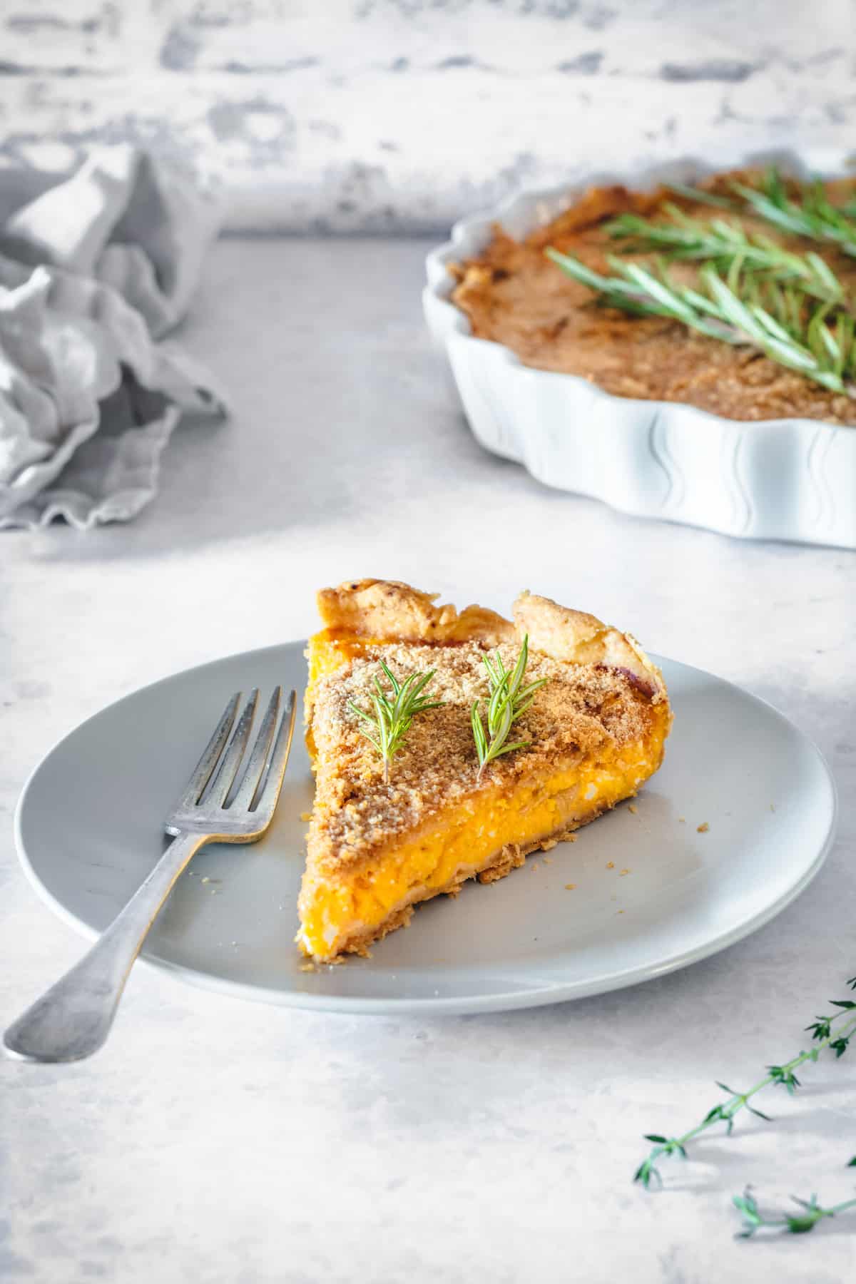 This Butternut Squash Tart with Caramelized Onions features creamy squash and a variety of cheeses. Perfect for fall holidays! A slice of butternut squash tart with caramelized onions on a white plate