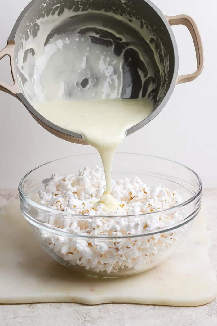 Pouring marshmallow mixture into bowl of popcorn.