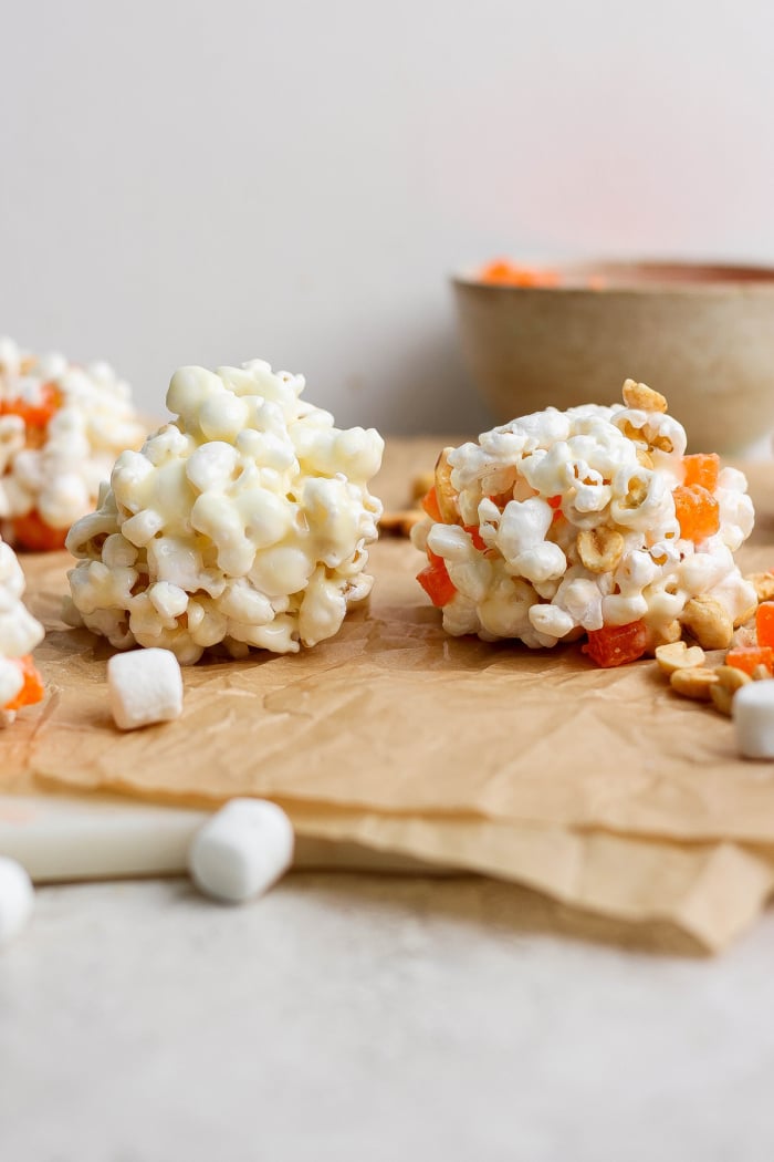 Two homemade marshmallow popcorn balls on parchment paper.