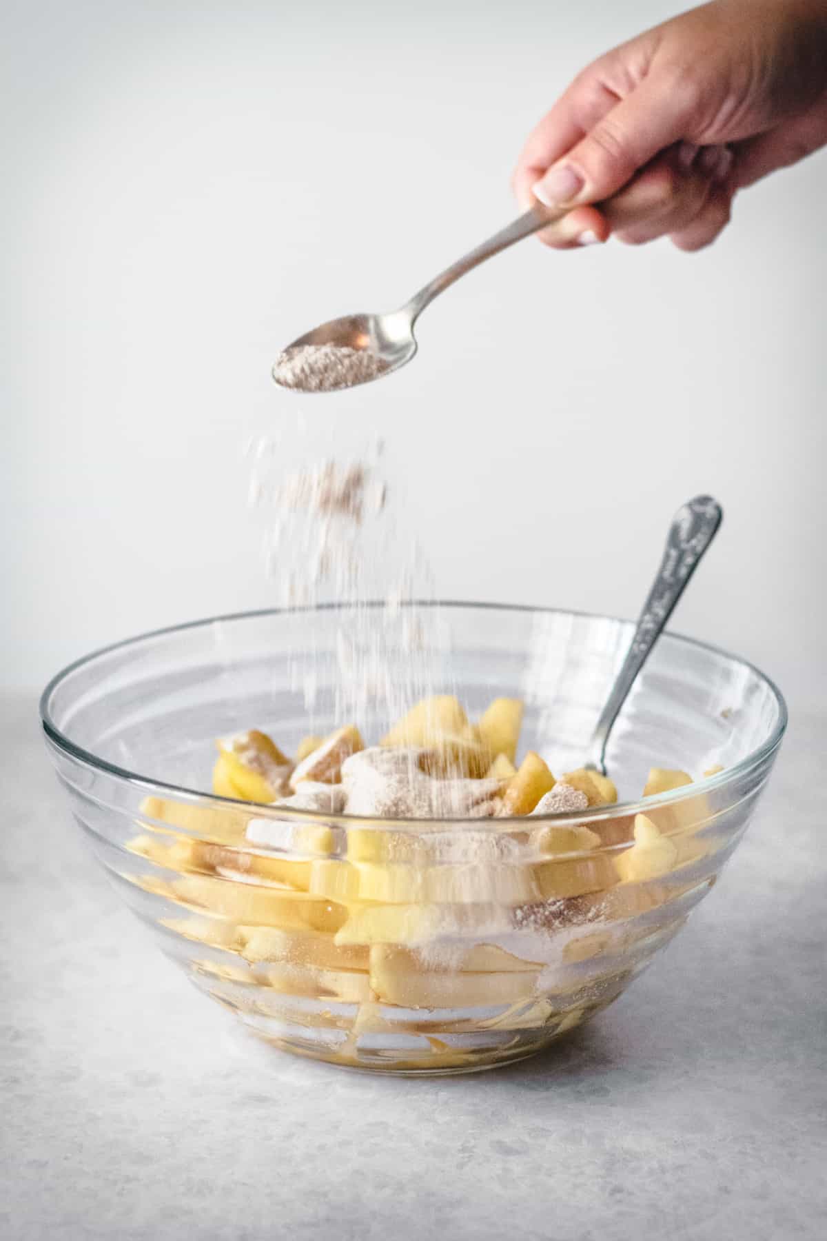 Cinnamon being added to a bowl of apple slices