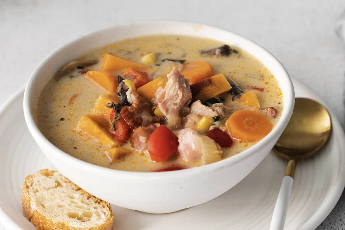 Close up of a bowl of smokedturkey chowder with a piece of crusty bread