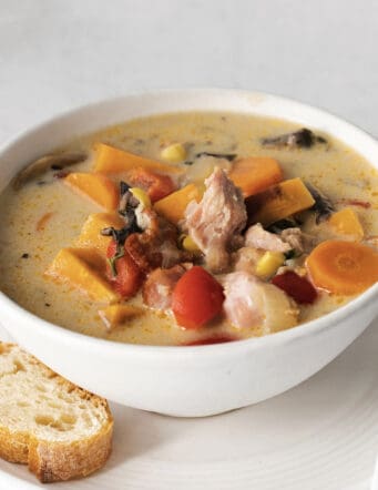 Close up of a bowl of leftover turkey chowder with a piece of crusty bread