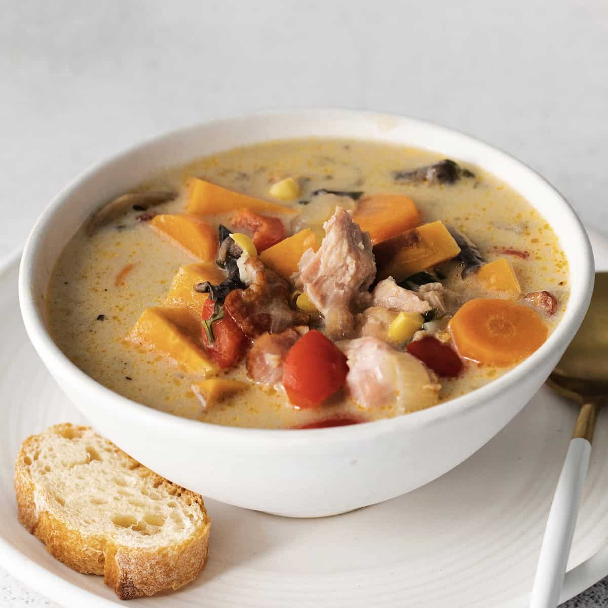 Close up of a bowl of leftover turkey chowder with a piece of crusty bread