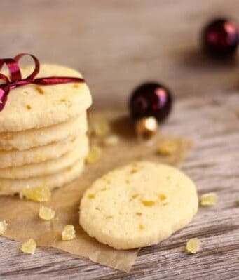 A stack of shortbread cookies with pieces of candied ginger wrapped in plum-colored ribbon