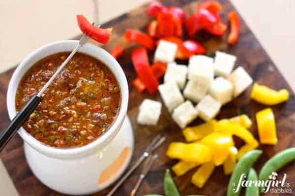 Bagna Cauda dip with sun-dried tomatoes in a warming pot with vegetables and bread cubes for dipping