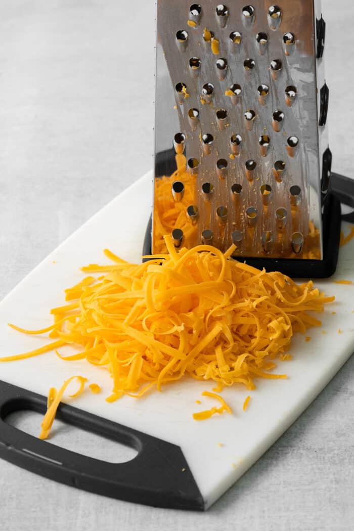 Freshly shredded cheddar cheese next to a cheese grater