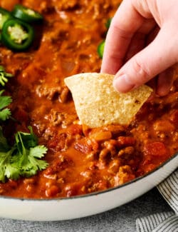 A tortilla chip digging into cheesy taco dip