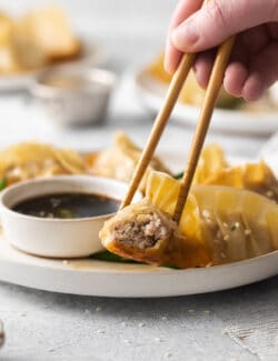 Chopsticks holding a piece of potsticker dipped in sauce