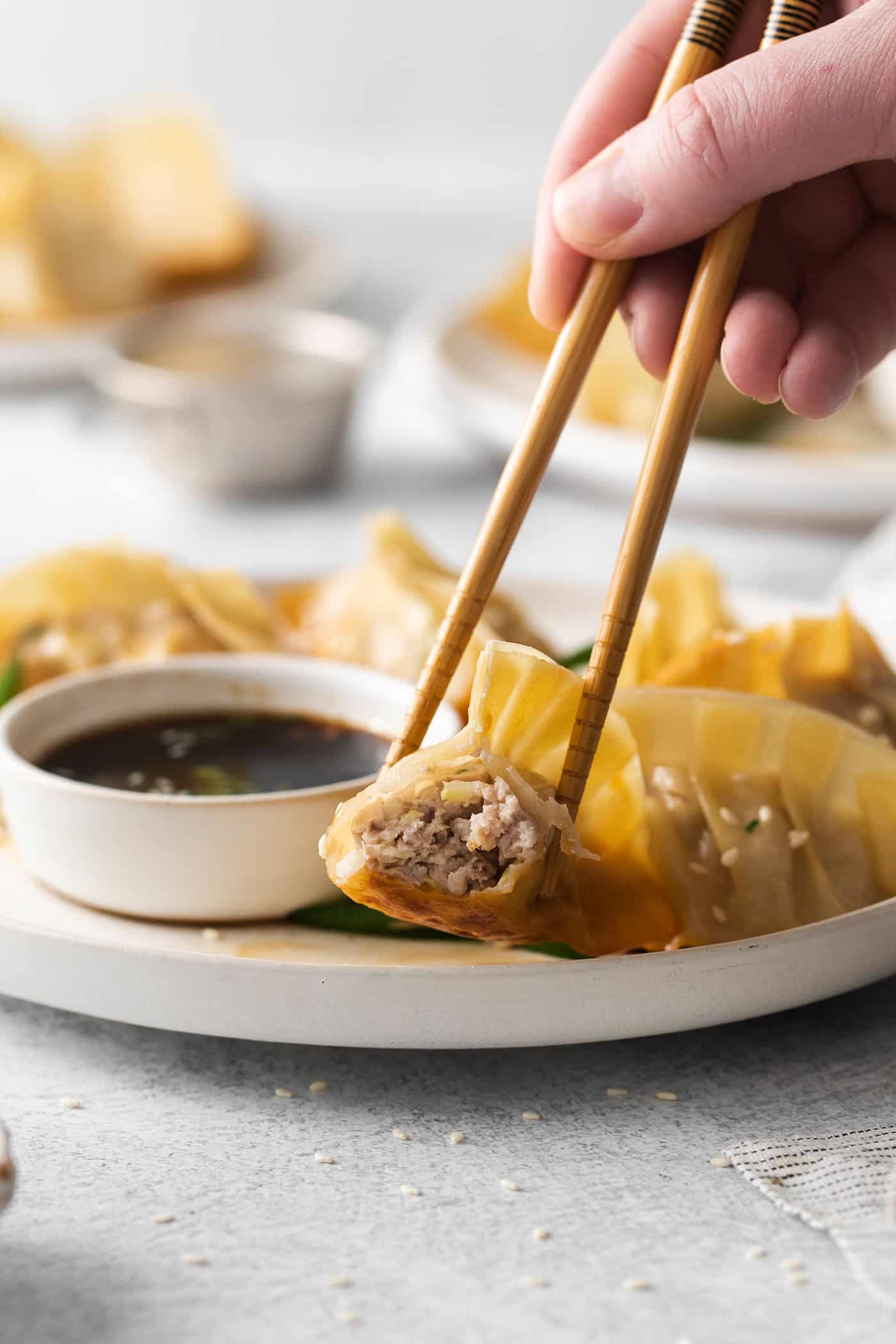 Chopsticks holding a piece of potsticker dipped in sauce