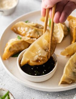 Chopsticks dipping a potsticker into sauce