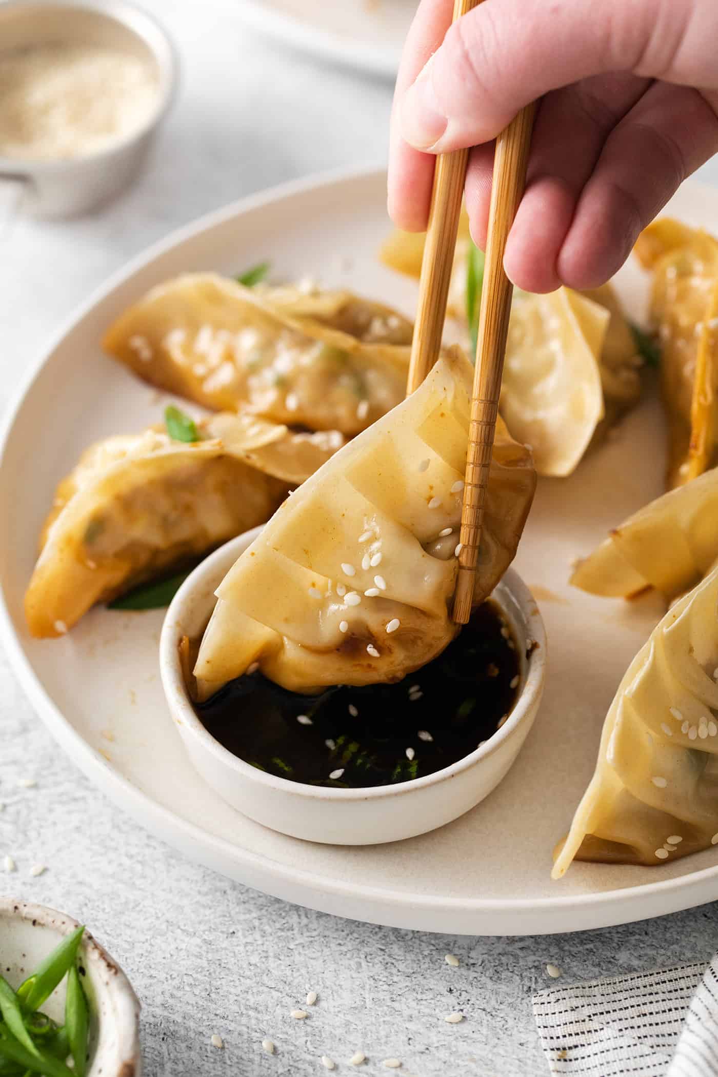 Chopsticks dipping a potsticker into sauce