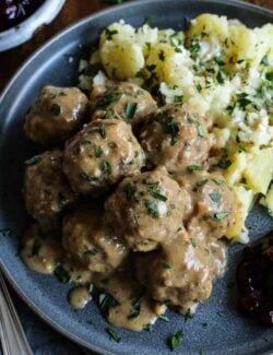 Swedish meatballs with gravy on a gray plate, with potatoes and lingonberry jam