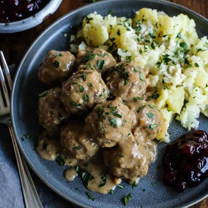 Swedish meatballs with gravy on a gray plate, with potatoes and lingonberry jam