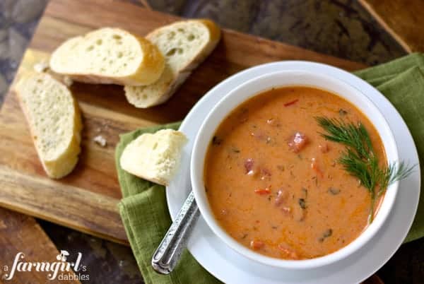 a white bowl of tomato bisque with pieces of bread