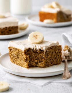 A slice of homemade banana cake on a plate with a bite missing