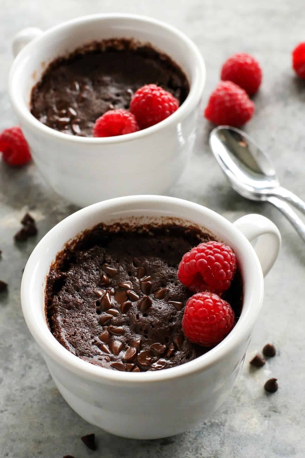 two white mugs of chocolate cake with fresh raspberries