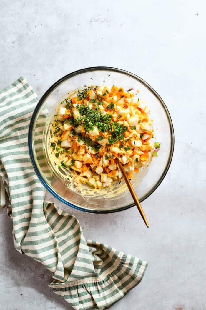 Spoon in bowl of ingredients for egg salad.