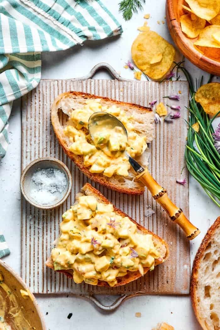 Spoon set on slice of bread topped with creamy egg salad.