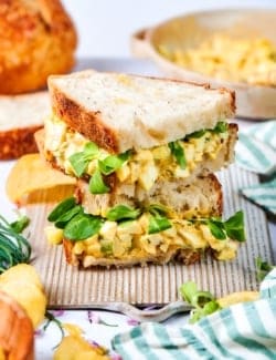 Two egg salad sandwich halves stacked on board.