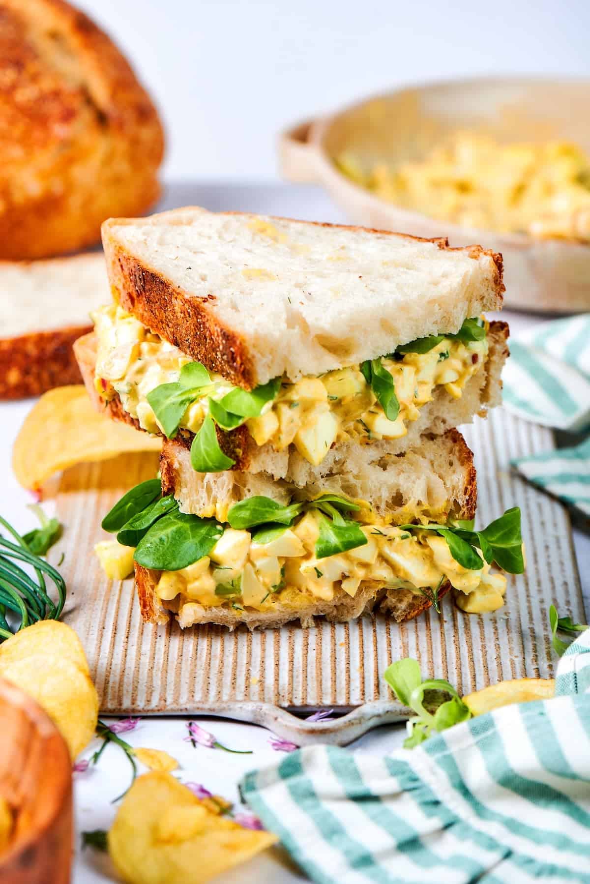 Two egg salad sandwich halves stacked on board.