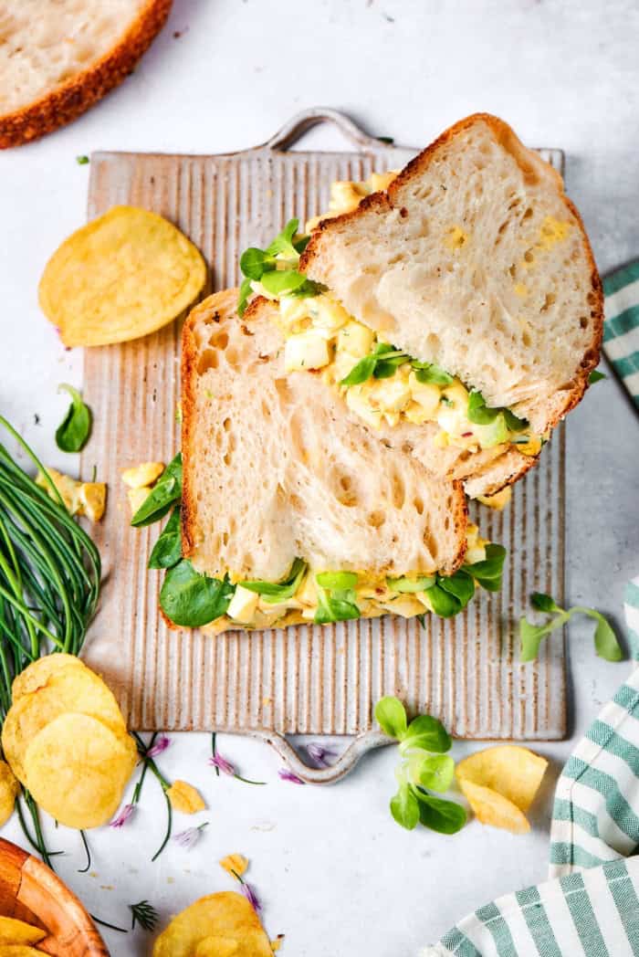 Two egg salad sandwich halves stacked on board.
