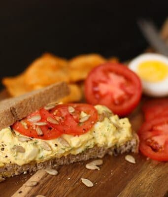 A piece of bread topped with herby egg salad and tomatoes