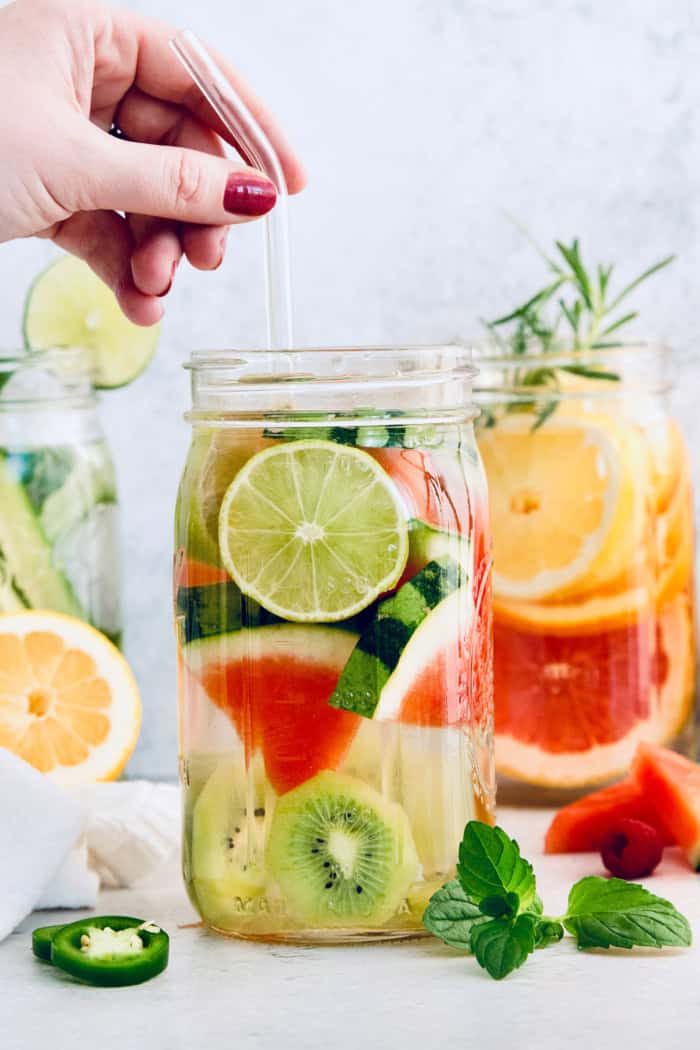 Hand holding glass straw in jar of spa water with kiwi, lime, and watermelon
