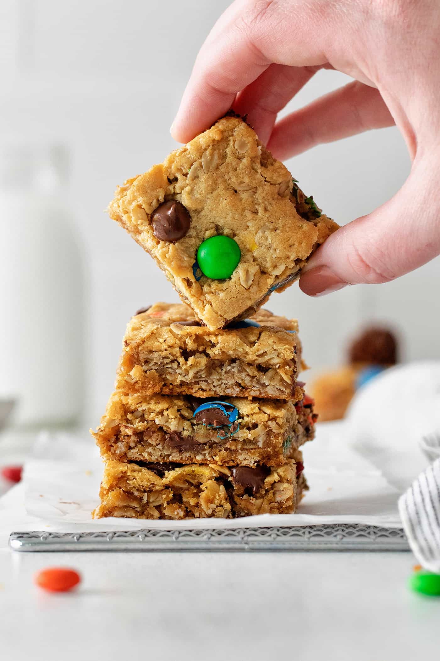 A hand picking up the top cookie bar from a stack of monster cookie bars