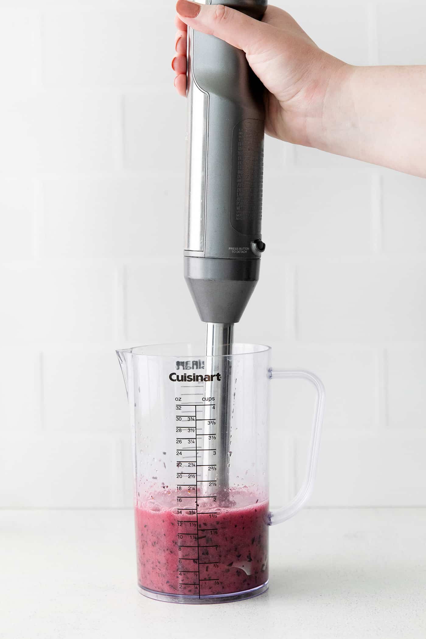 An immersion blender blending blueberries