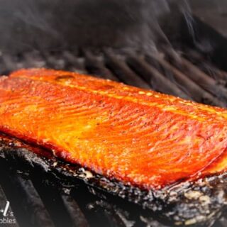 A browned side of salmon cooking on a grill