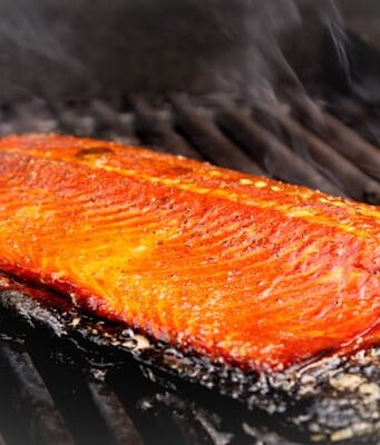 A browned side of salmon cooking on a grill