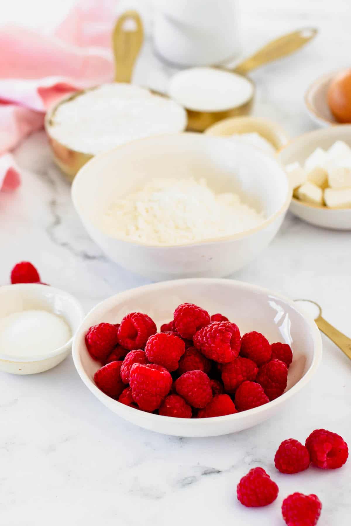 A white bowl of raspberries and a white bowl of flour