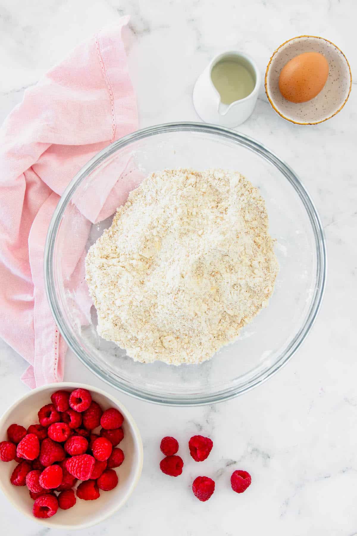 The dry ingredients for drop scones in a mixing bowl and a bowl for raspberries