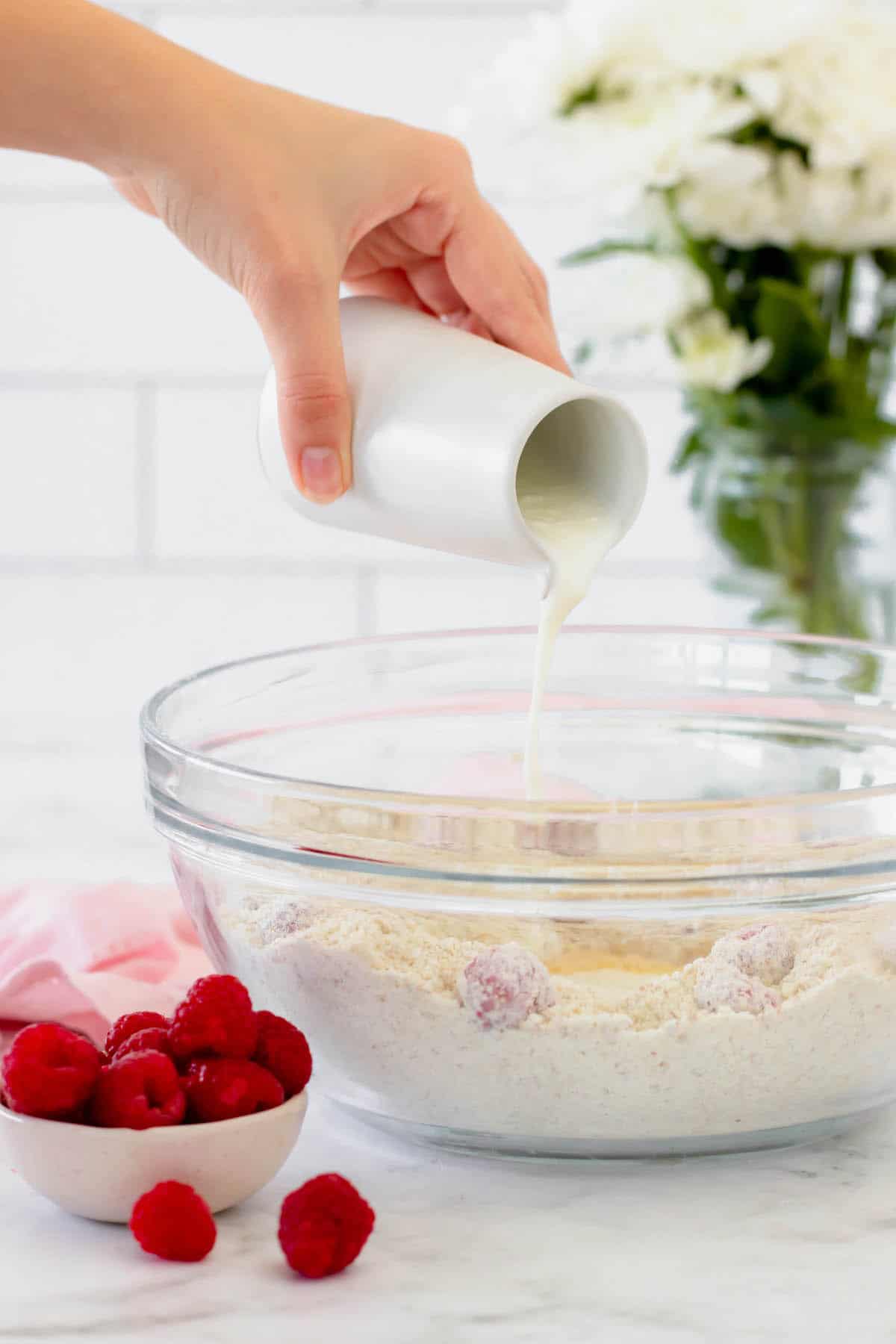 A hand pouring buttermilk into a mixing bowl