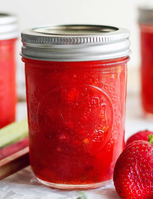 Jar of strawberry rhubarb freezer jam with fresh strawberries and rhubarb stalks
