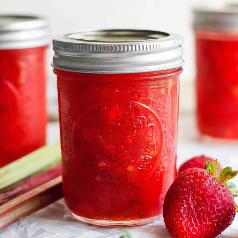 Jar of strawberry rhubarb freezer jam with fresh strawberries and rhubarb stalks