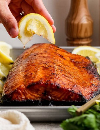 Hand squeezing lemon wedge over sweet and smoky grilled salmon
