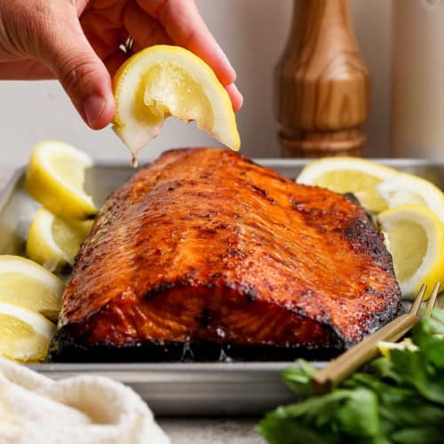 Hand squeezing lemon wedge over sweet and smoky grilled salmon