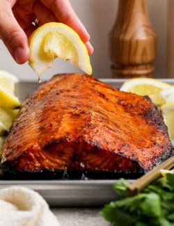 Hand squeezing lemon wedge over sweet and smoky grilled salmon