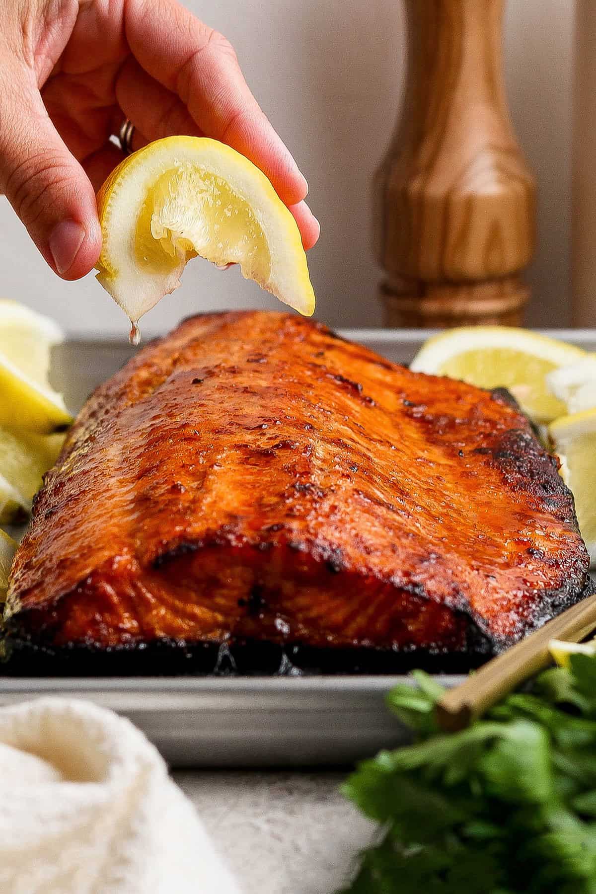 Hand squeezing lemon wedge over sweet and smoky grilled salmon