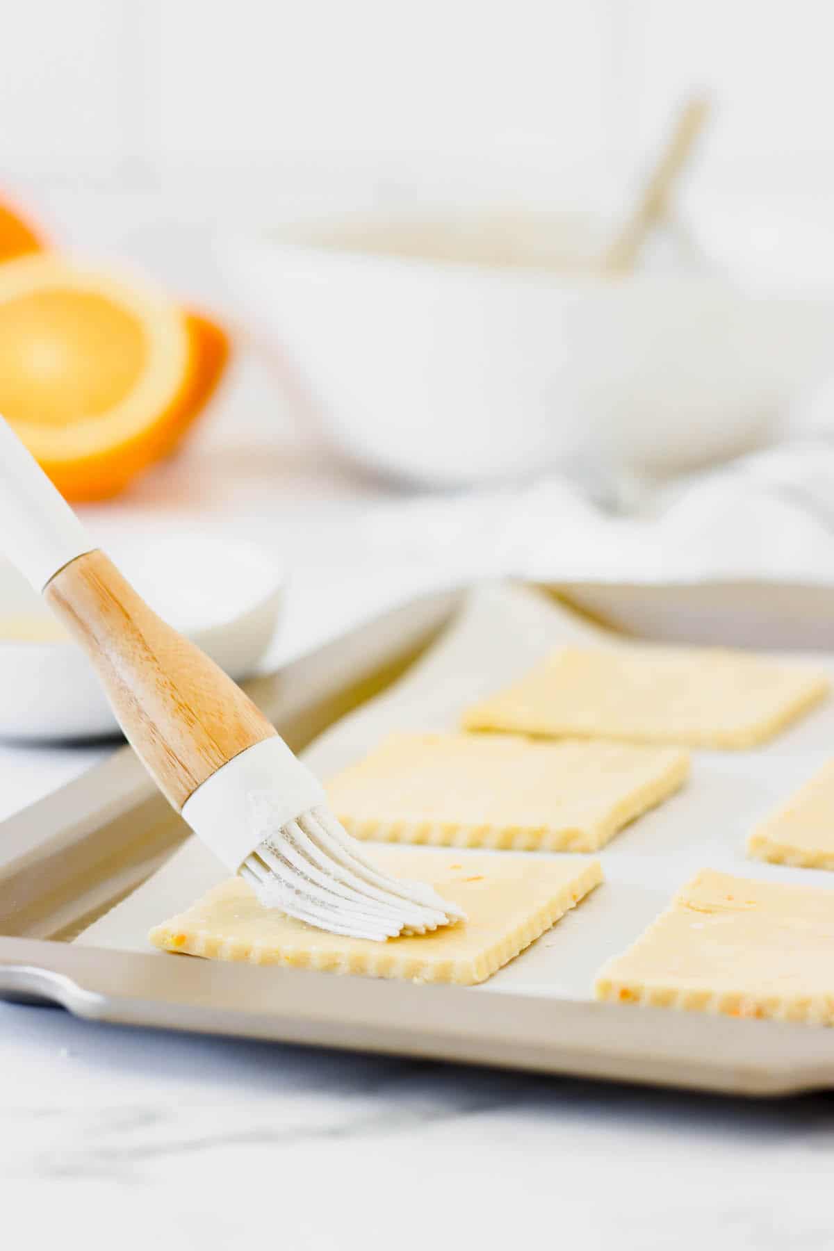 Pastry dough cut into squares being glazed with an egg wash on a baking sheet