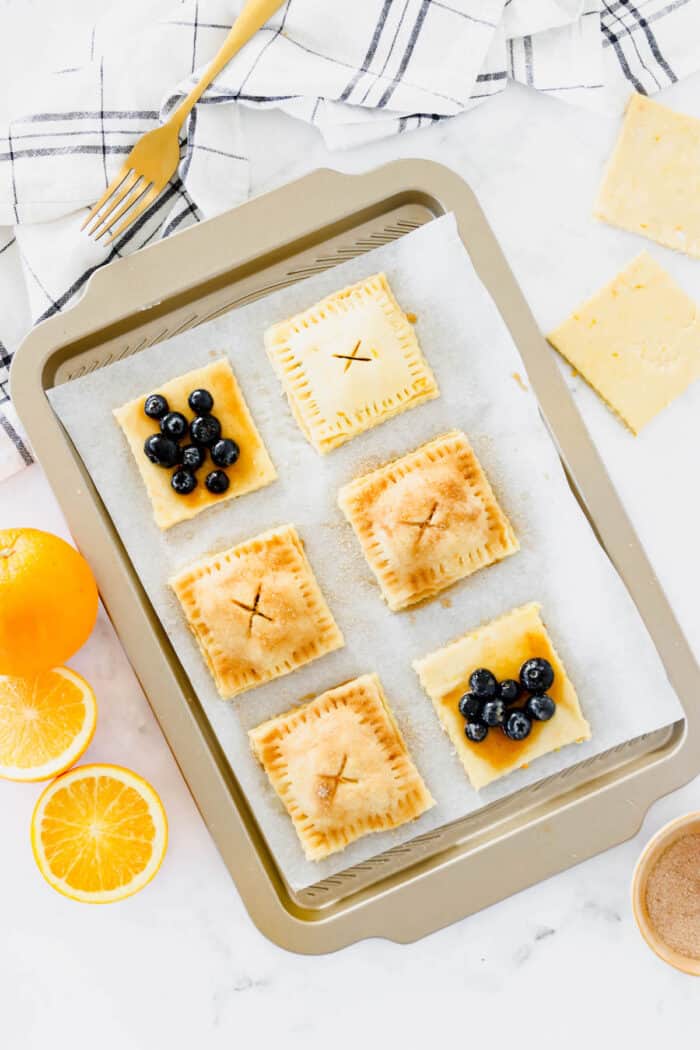 Overhead view of partially assembled blueberry hand pies on a lined baking sheet.