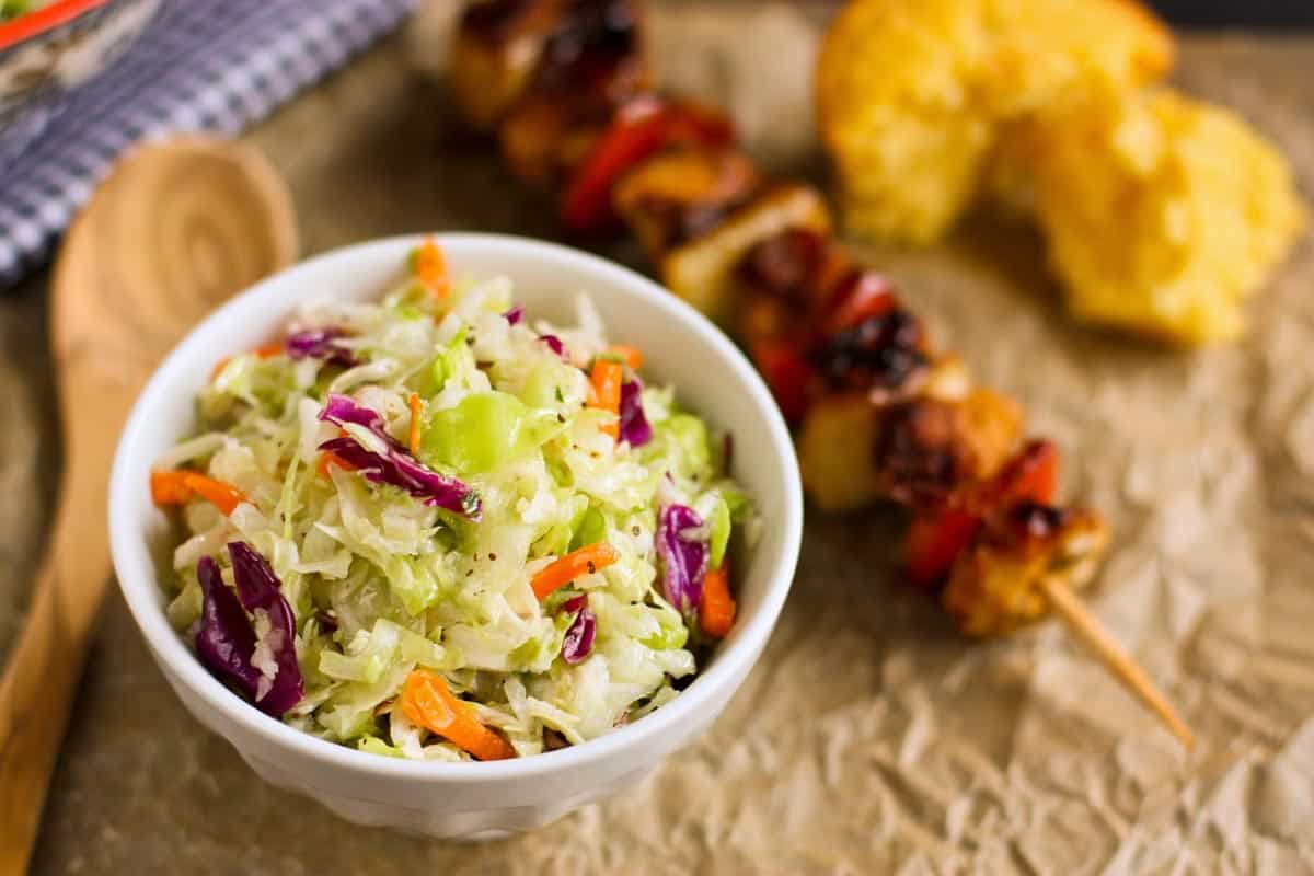 coleslaw salad in a small white bowl, chicken kebab, and cornbread muffin