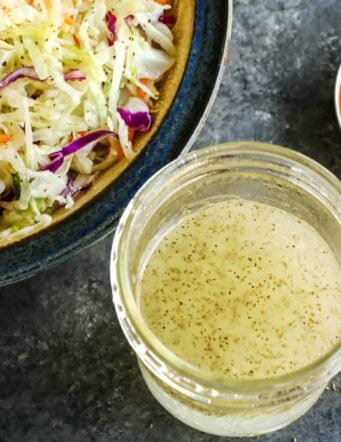 a jar of vinegar coleslaw dressing and a bowl of shredded cabbage