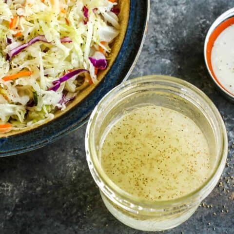 a jar of vinegar coleslaw dressing and a bowl of shredded cabbage