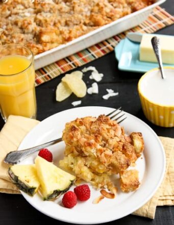 Coconut-Ginger Baked French Toast on a white plate with fresh pineapple and raspberries
