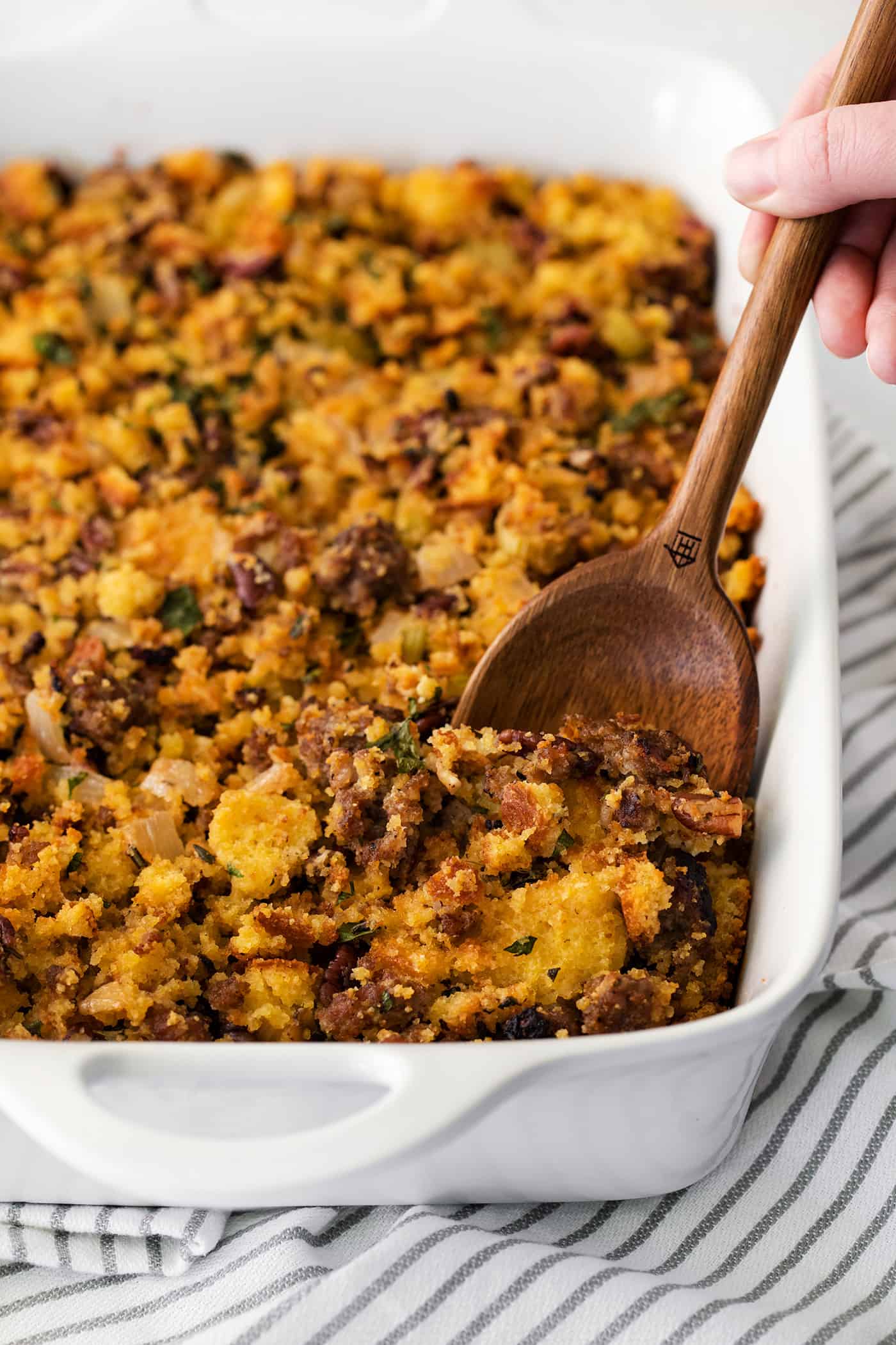 A wooden spoon serving cornbread dressing in a white casserole dish