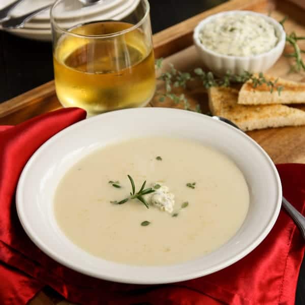 A white bowl of creamy potato soup topped with fresh herb compound butter