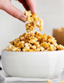 A hand crabbing a piece of caramel popcorn from a white bowl