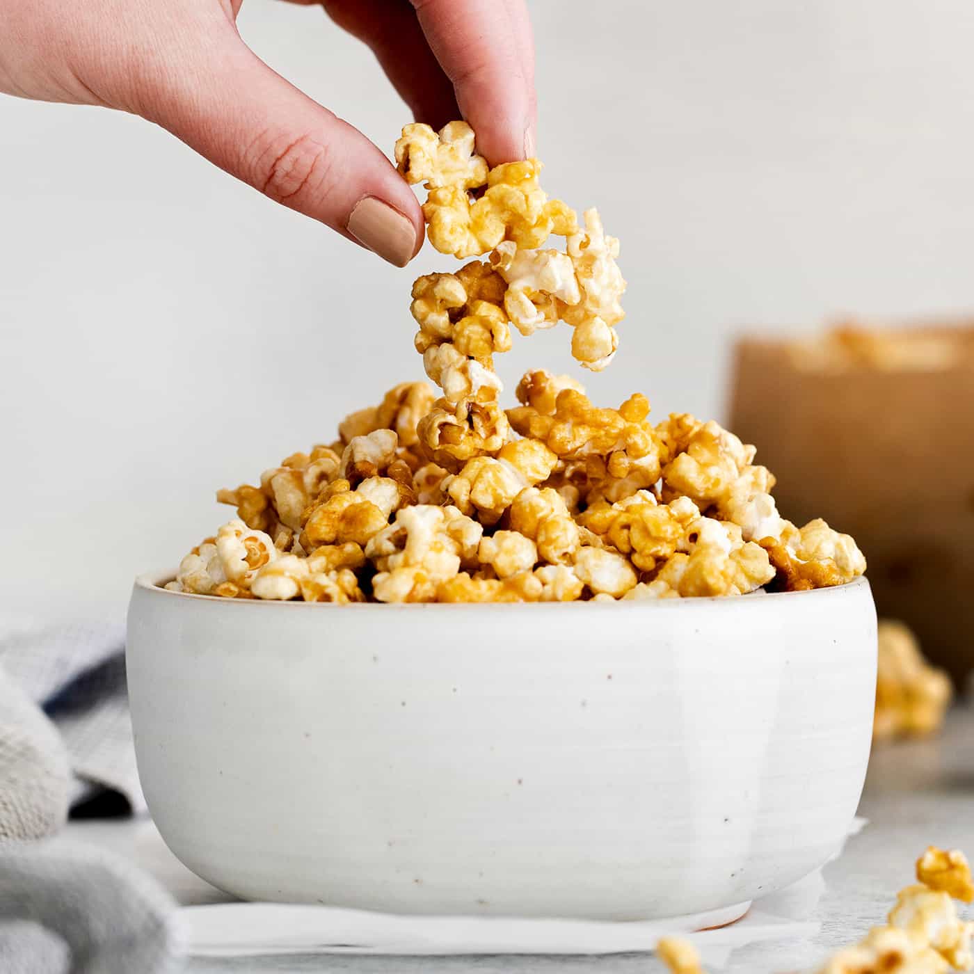 A hand crabbing a piece of caramel popcorn from a white bowl